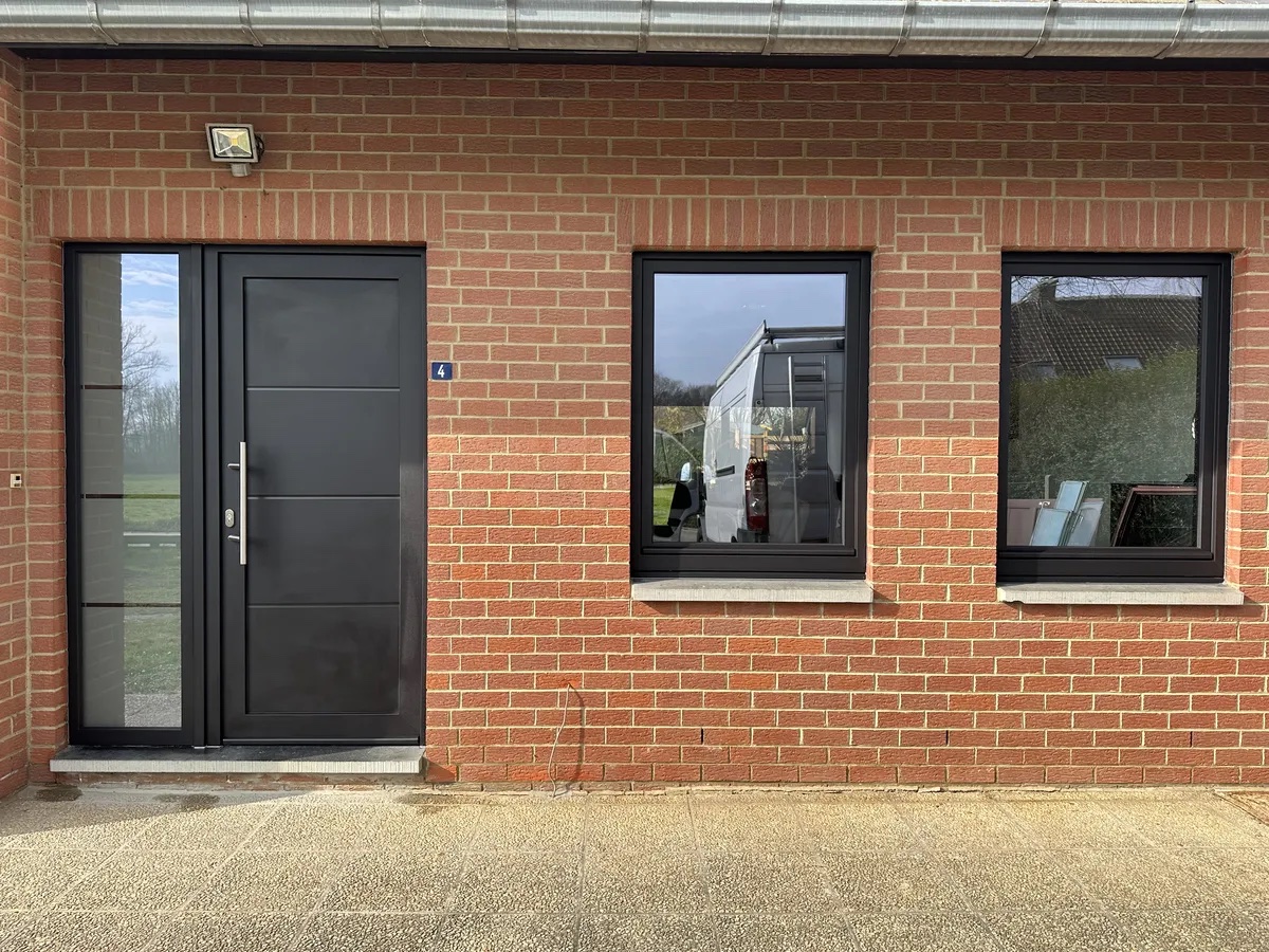 Porte et fenêtres en aluminium anthracite sur une façade en brique rouge, réalisation Menuiserie Bedetti à Gosselies