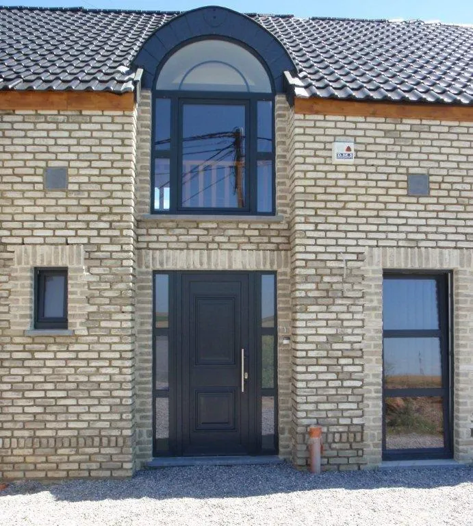 Porte d'entrée en aluminium noir et imposte vitrée sur une façade en brique claire, réalisation FT Châssis en Hainaut