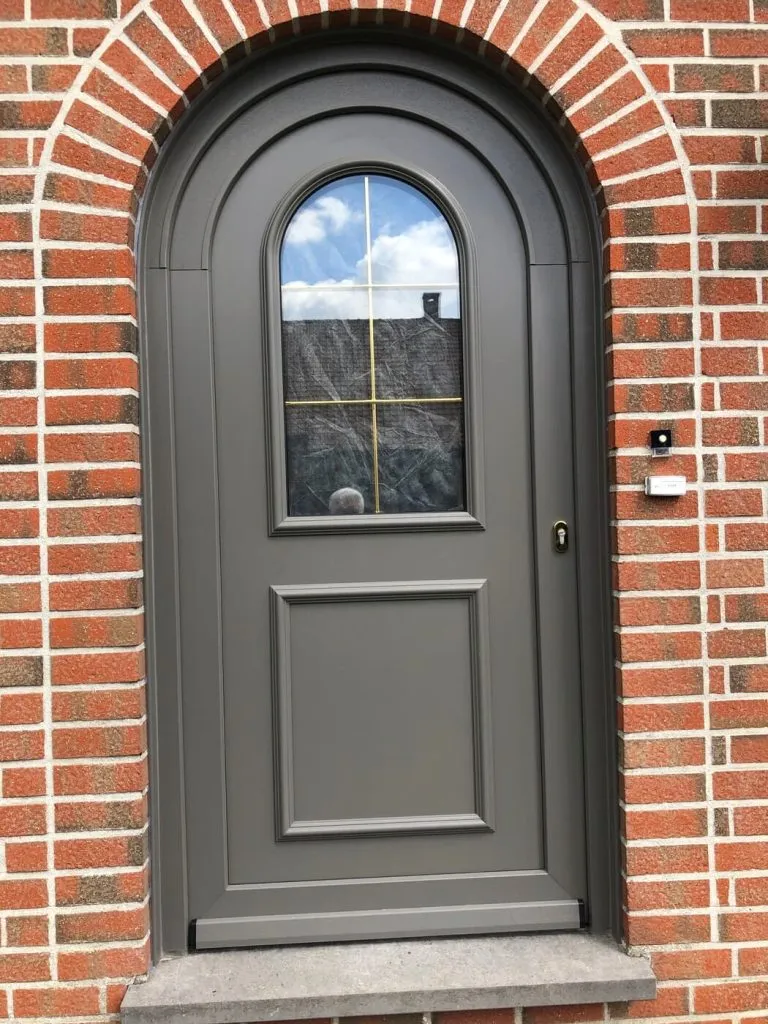 Porte d'entrée cintrée gris anthracite sur une façade en brique, réalisation Menuiserie Kenan