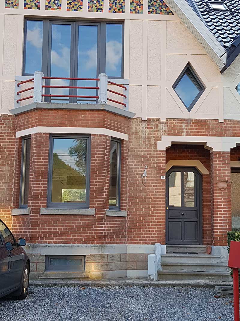 Châssis anthracite, fenêtre losange et porte foncée sur une maison en brique avec bow-window, réalisation Menuiserie Audain & Fils