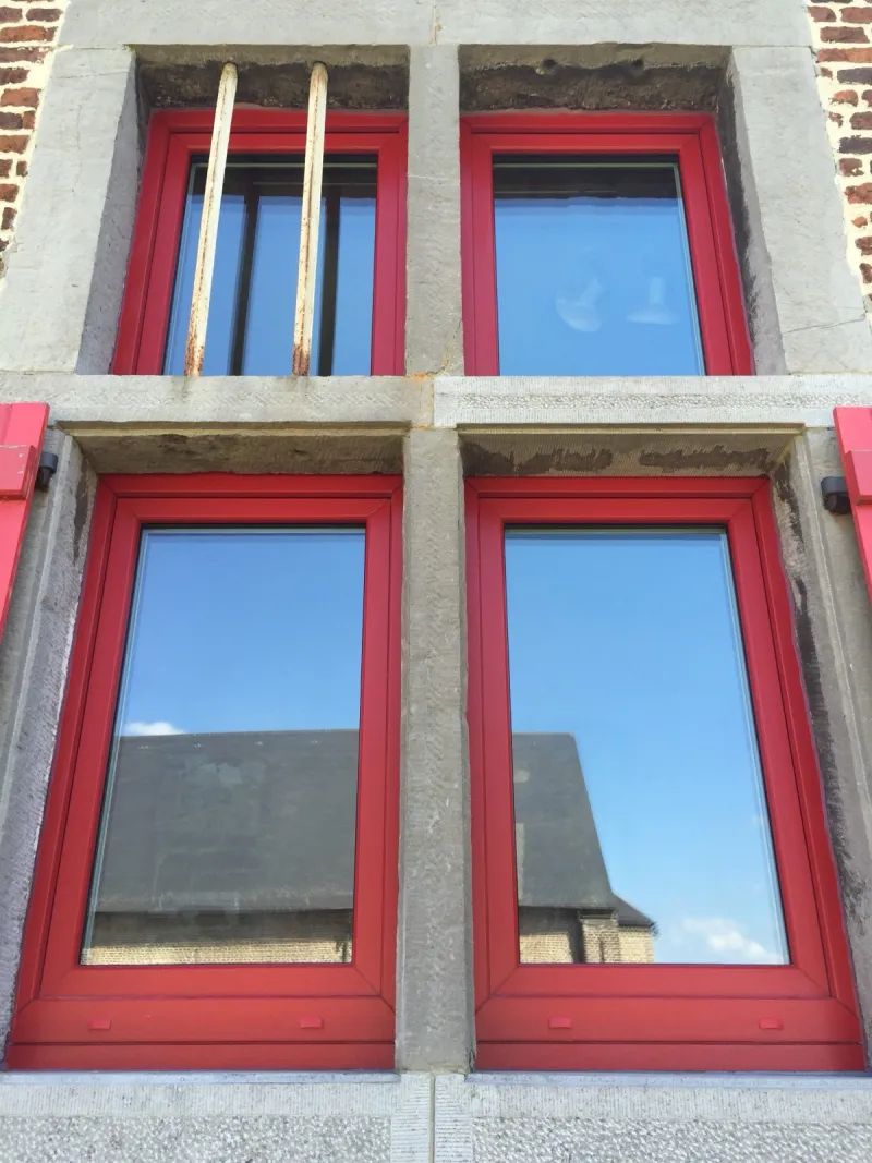 Châssis en teinte rouge posés sur une façade en pierre, réalisation MD Concept Home en province de Namur