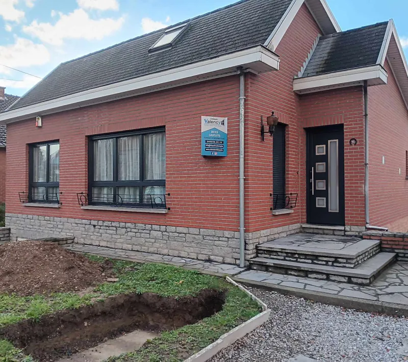 Châssis anthracite et porte d'entrée sur une villa en brique rouge sur soubassement en pierre, réalisation Châssis Valency en Hainaut