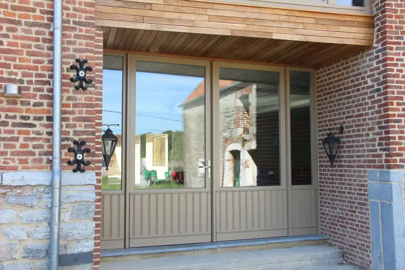Porte d'entrée et châssis en aluminium beige sur une fermette en brique et pierre, réalisation Maison Passion