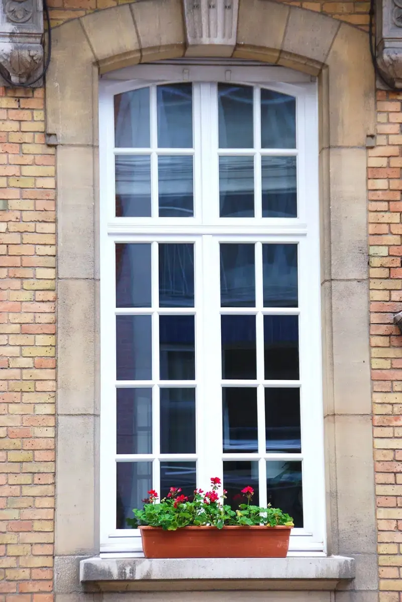 Haute fenêtre blanche à petits-bois encadrée de pierre sur une façade en brique claire, réalisation Maison Passion près de Namur
