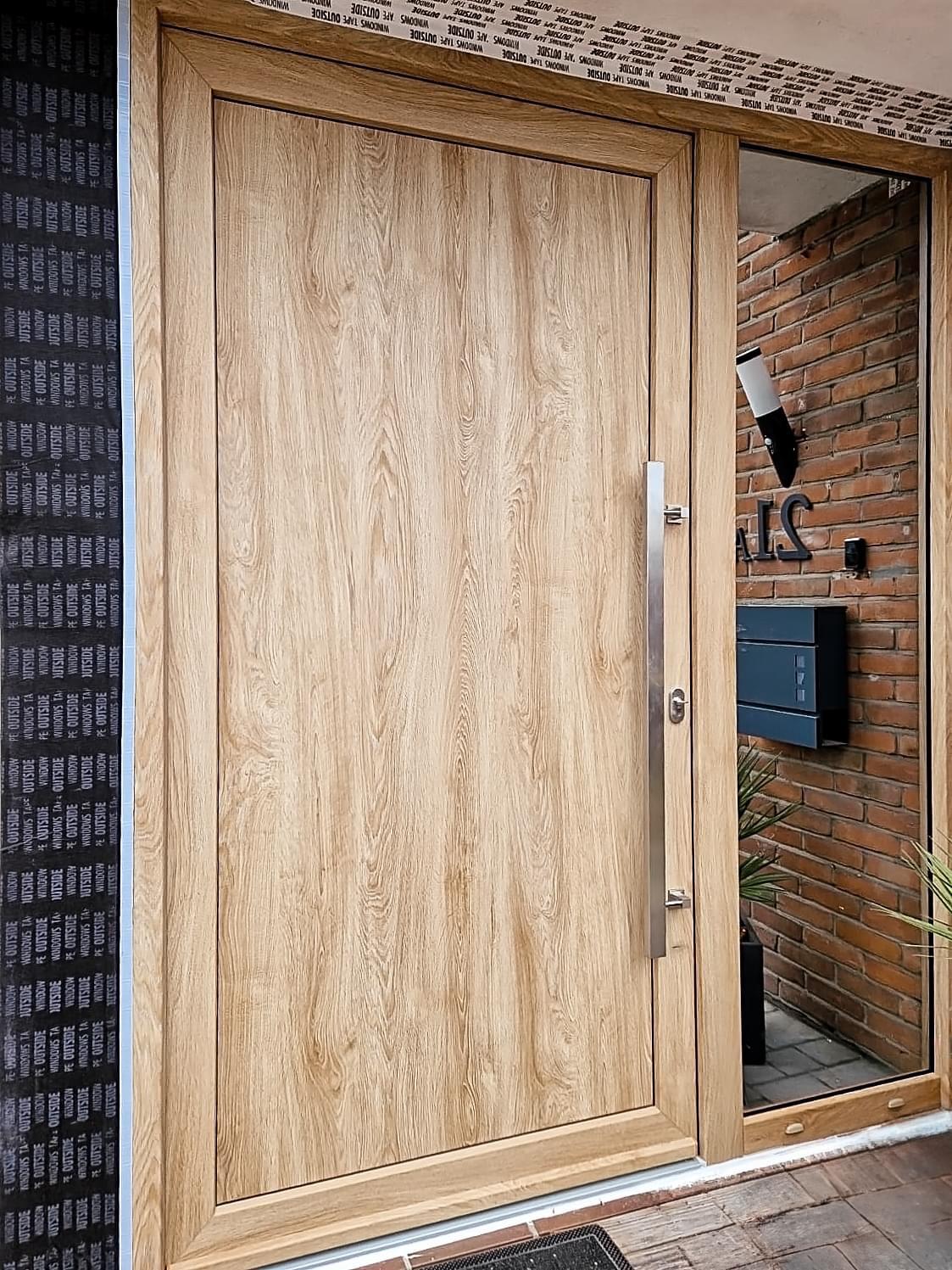 Porte d'entrée en aluminium aspect chêne avec panneau vitré latéral, fraîchement posée, réalisation Concepteo Châssis
