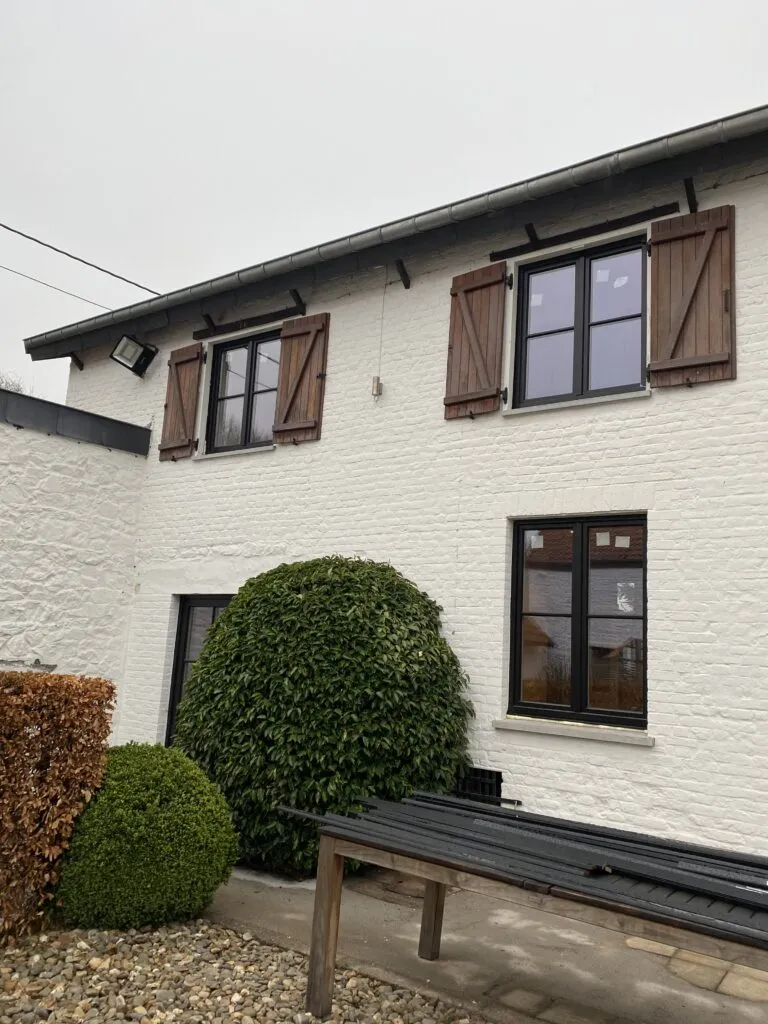 Châssis anthracite et volets en bois sur une maison à façade blanchie de la province de Namur, par SCID