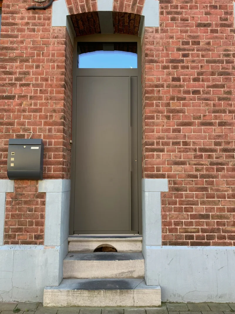Porte d'entrée taupe surmontée d'une imposte vitrée dans une façade en brique, réalisation SCID en province de Namur