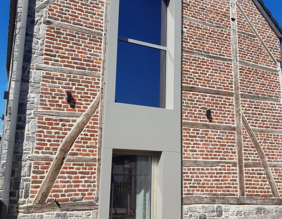 Grande fenêtre fixe posée sur un pignon ancien en pierre et brique, réalisation Gérégri en province de Liège