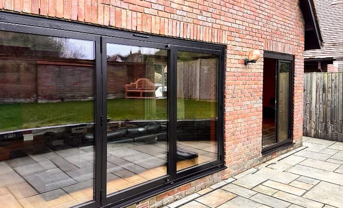 Baie coulissante et fenêtre en aluminium noir sur une façade en brique rouge avec terrasse, réalisation Sio2 Châssis à Flémalle