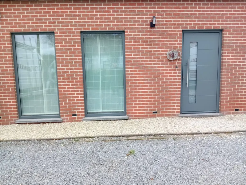 Deux châssis gris et porte d'entrée anthracite sur une façade en brique rouge, réalisation Menui'Deal dans la région de Mouscron