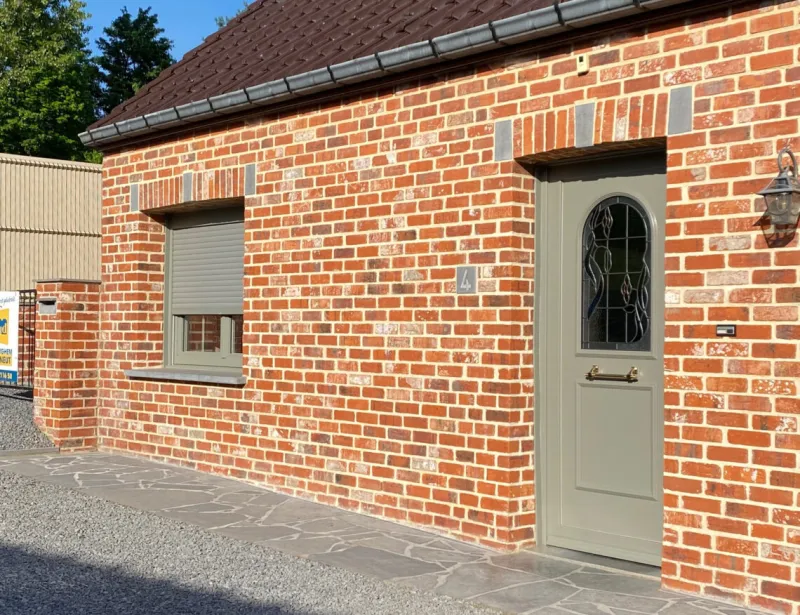 Porte d'entrée grise vitrée et fenêtre avec volet sur une maison en brique à Tournai, réalisation Menuiserie Morlighem - Decneut