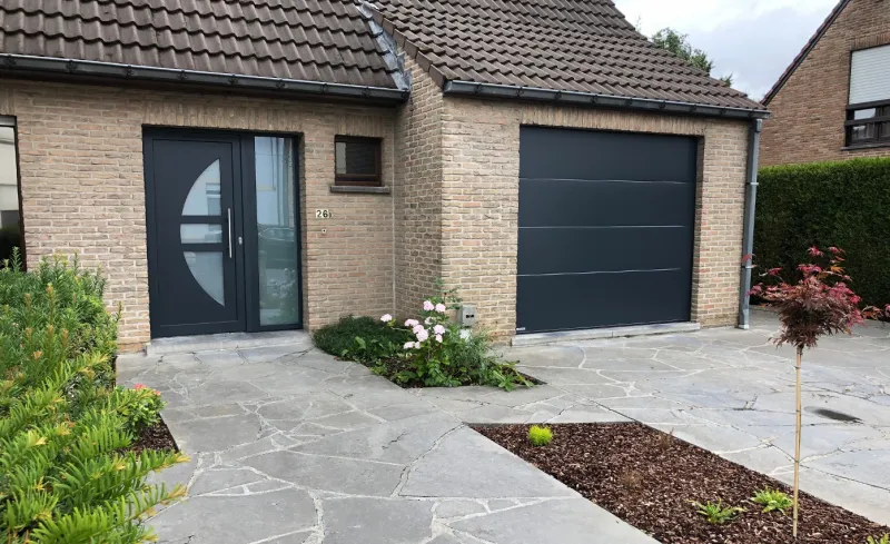 Porte d'entrée anthracite avec hublot vitré et fenêtre sur un bungalow en brique claire à Tournai, réalisation Menuiserie Morlighem - Decneut