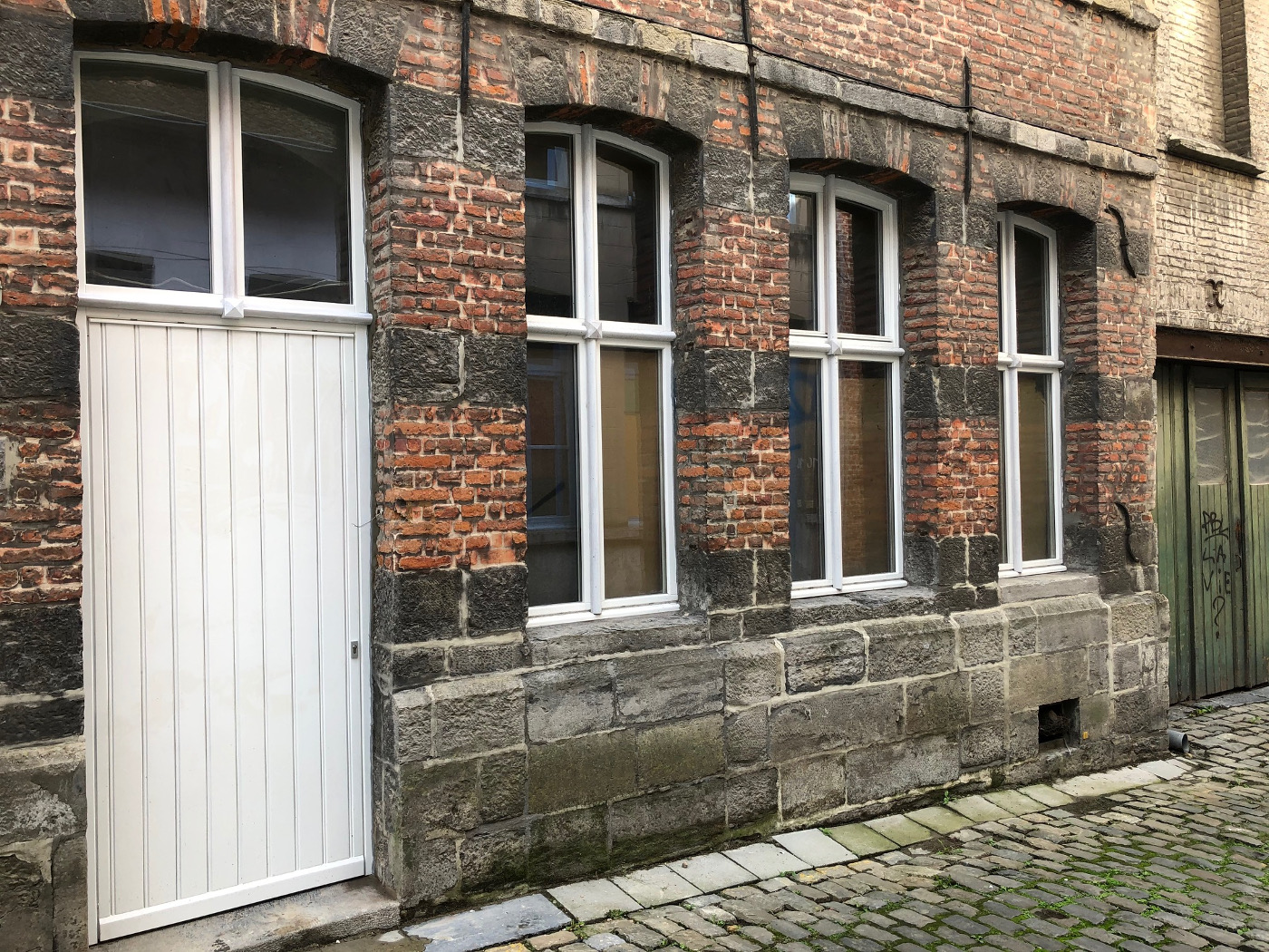 Fenêtres blanches à petits-bois et porte sur une vieille façade en pierre et brique du centre de Tournai, réalisation Menuiserie Morlighem - Decneut