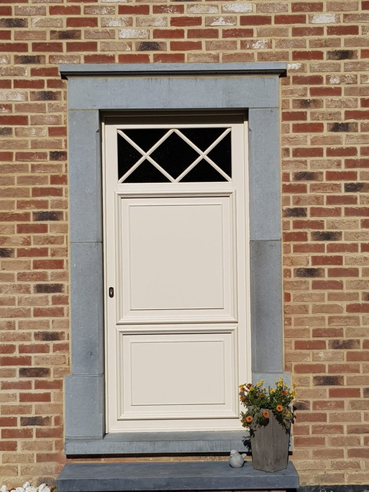 Porte d'entrée ivoire à imposte croisillonnée sur une façade en brique et pierre bleue, réalisation Chassis One à Wavre