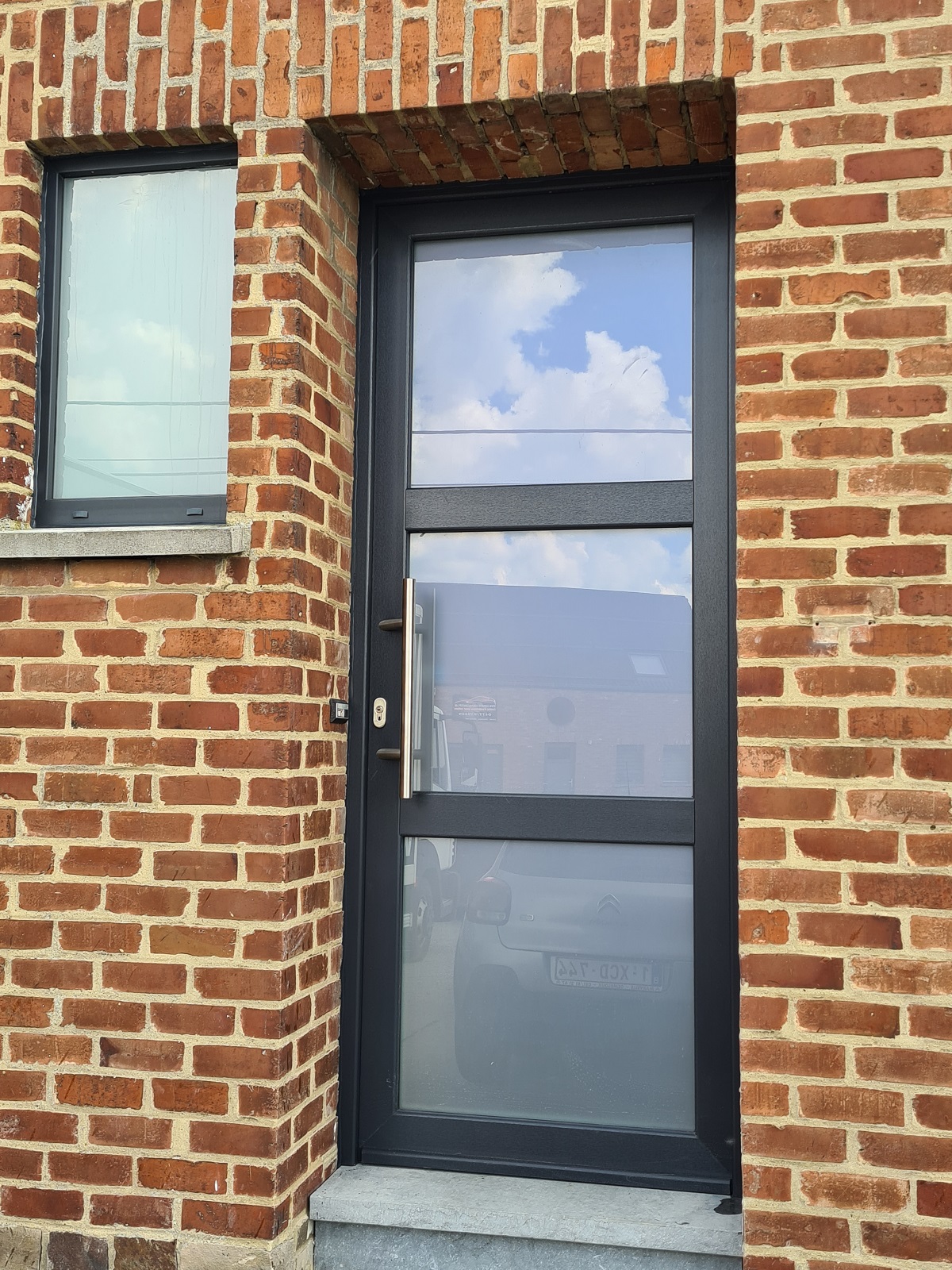 Porte d'entrée vitrée anthracite et fenêtre sur une façade en brique, réalisation Menuiserie MGPC dans la région de Wavre