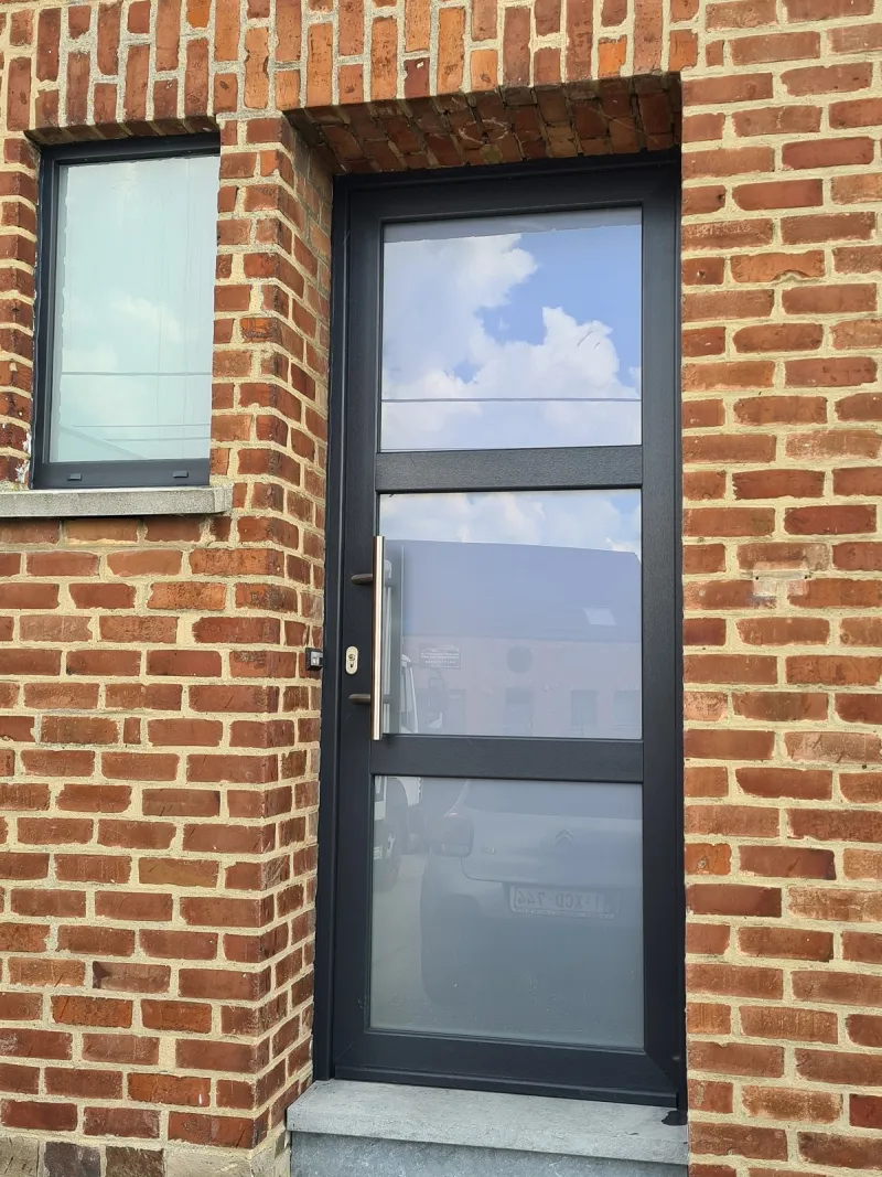 Porte d'entrée vitrée anthracite et fenêtre sur une façade en brique, réalisation Menuiserie MGPC dans la région de Wavre