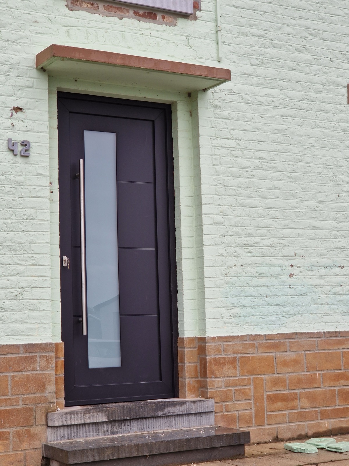 Porte d'entrée anthracite à bandeau vitré sur une façade en brique peinte, réalisation Menuiserie Paten en Brabant wallon