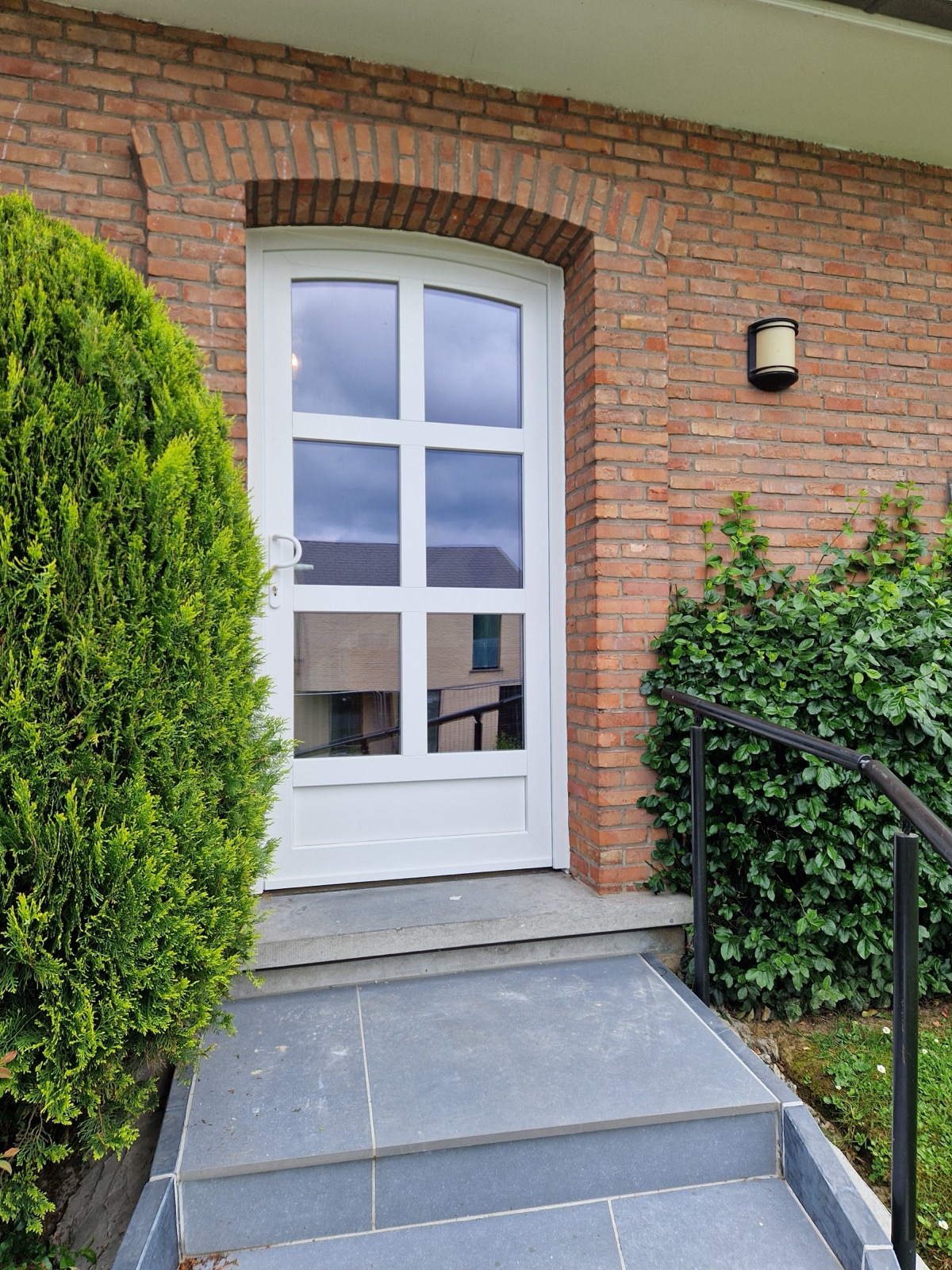 Porte d'entrée vitrée blanche à petits-bois sur une façade en brique avec seuil en pierre bleue, réalisation Menuiserie Paten
