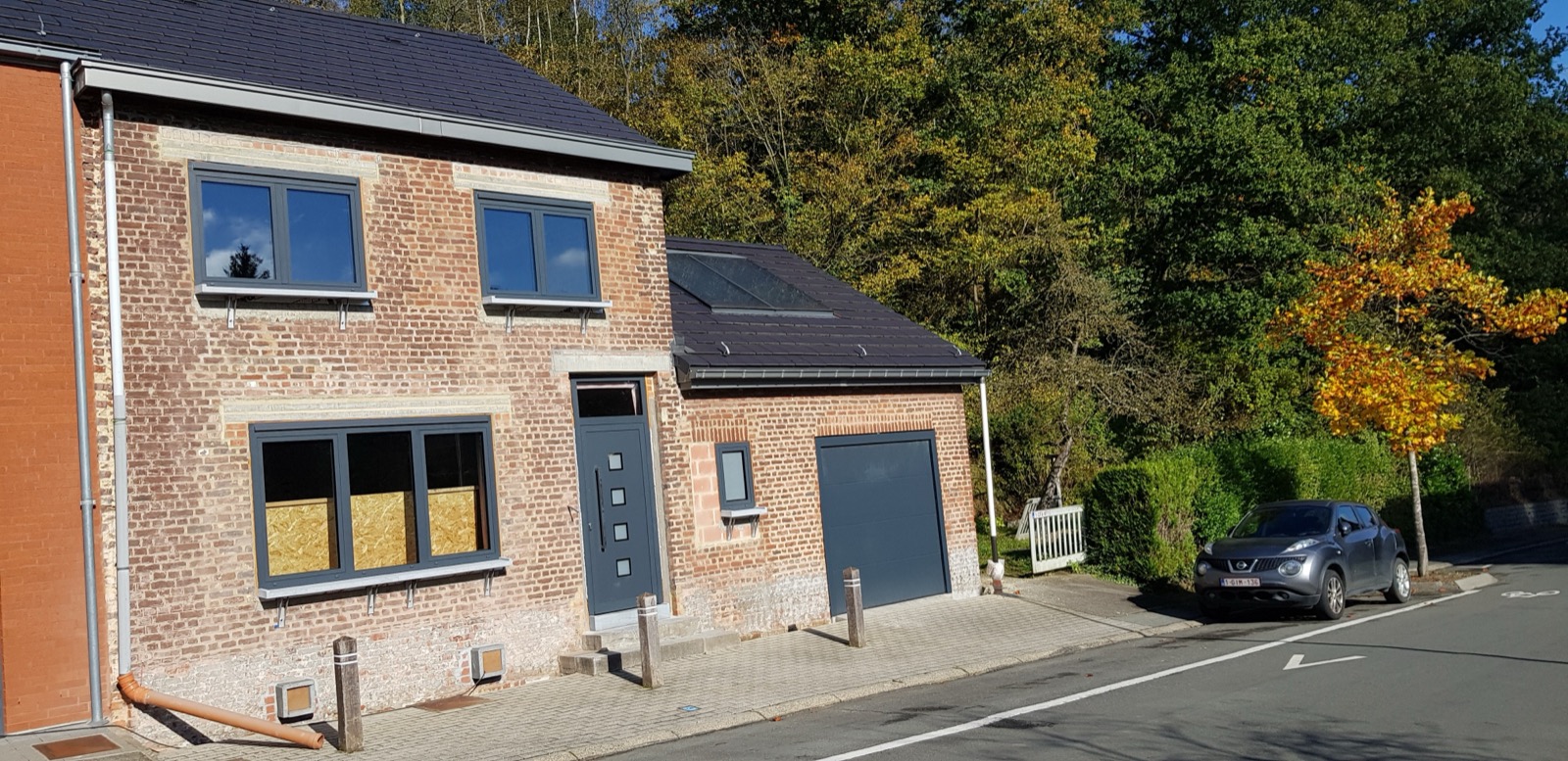 Maison quatre façades en brique avec châssis gris, porte d'entrée et porte de garage neufs, réalisation Menuiserie Paten en Brabant wallon