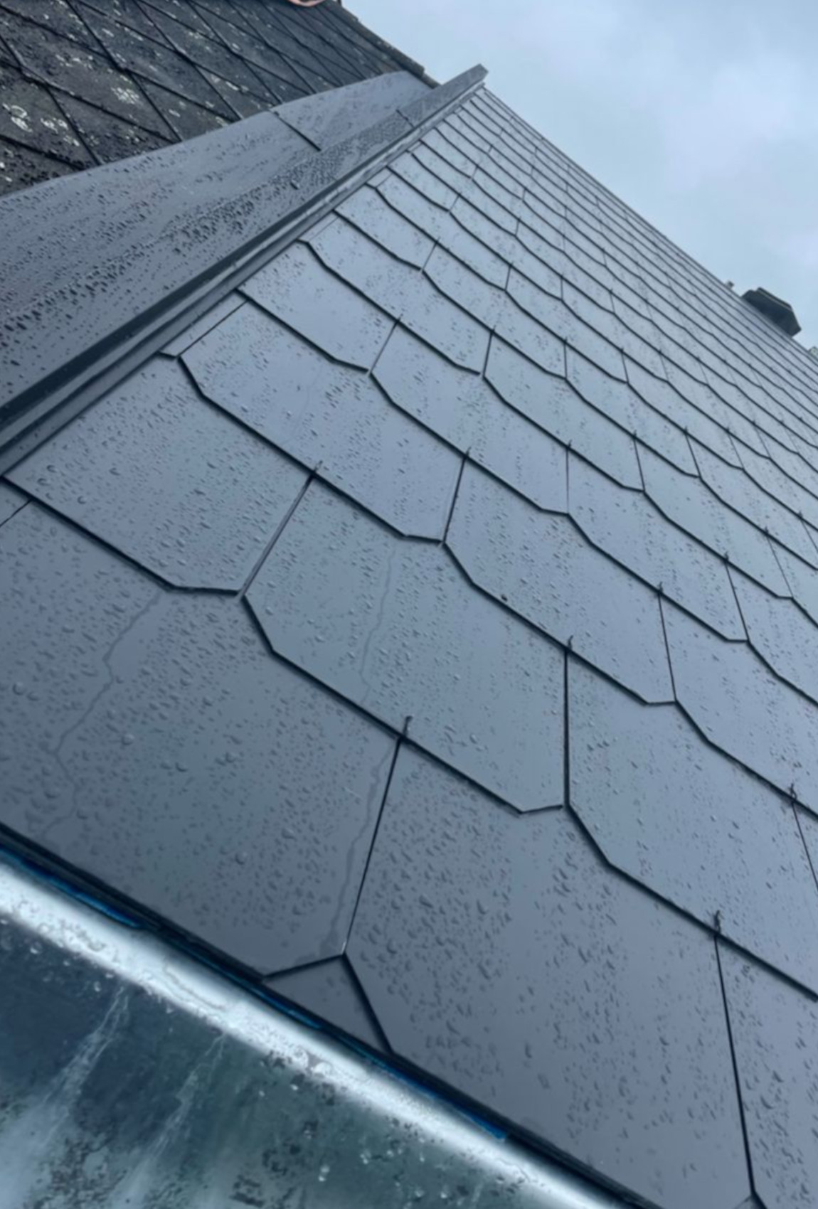 Versant de toiture en ardoises avec arêtier et bavette en zinc réalisé par Bougha Toitures