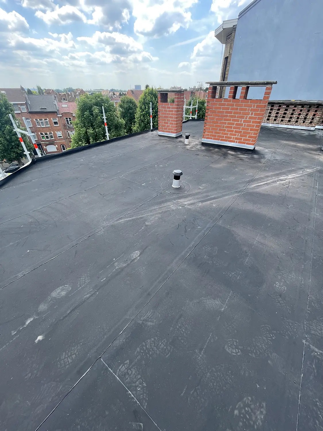 Toiture plate en EPDM avec souches de cheminée et vue sur les toits bruxellois, par Delta-X Toitures