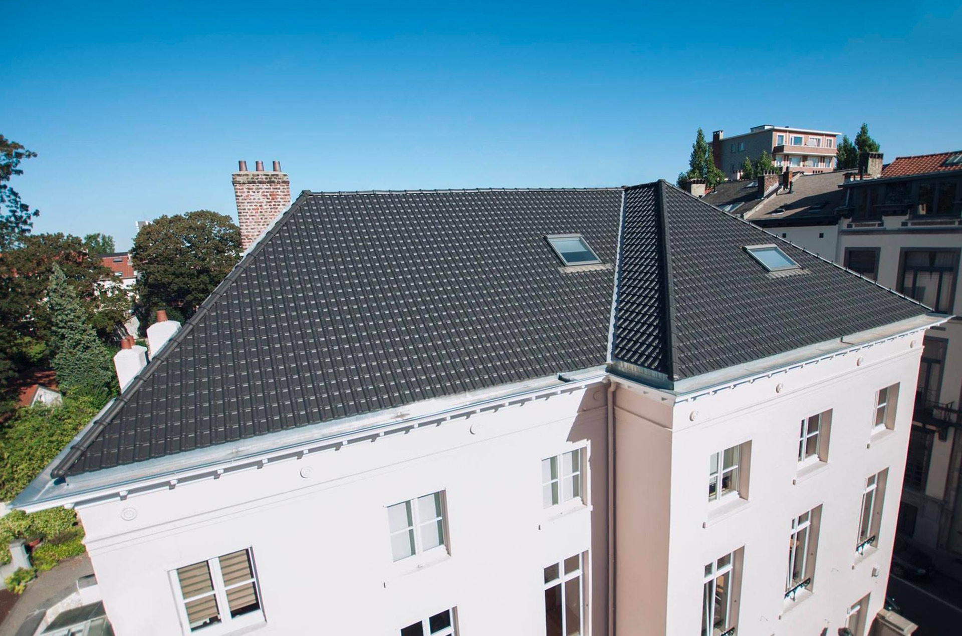Toiture en tuiles émaillées noires avec fenêtres de toit et vue sur les toits bruxellois, par Toiture DIM